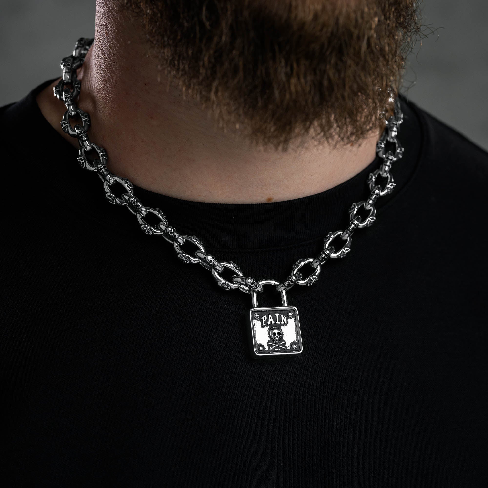 Silver skull chain with padlock pendant with skull and word "pain" embedded above skull, on male model 