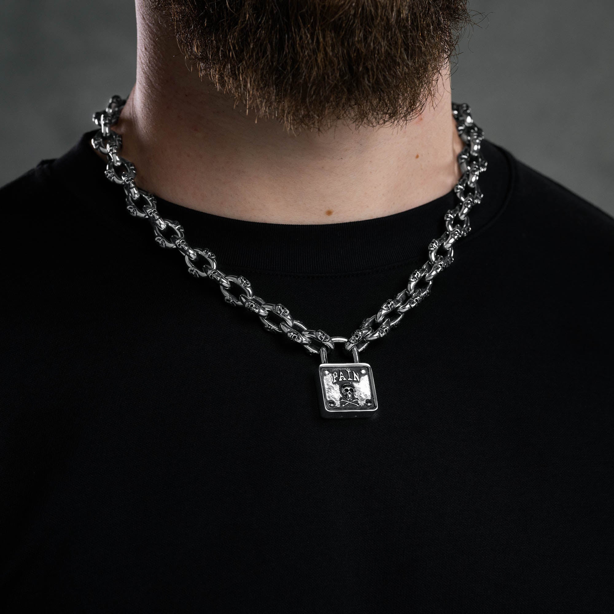 Silver skull chain with padlock pendant with skull and word "pain" embedded above skull, on male model 