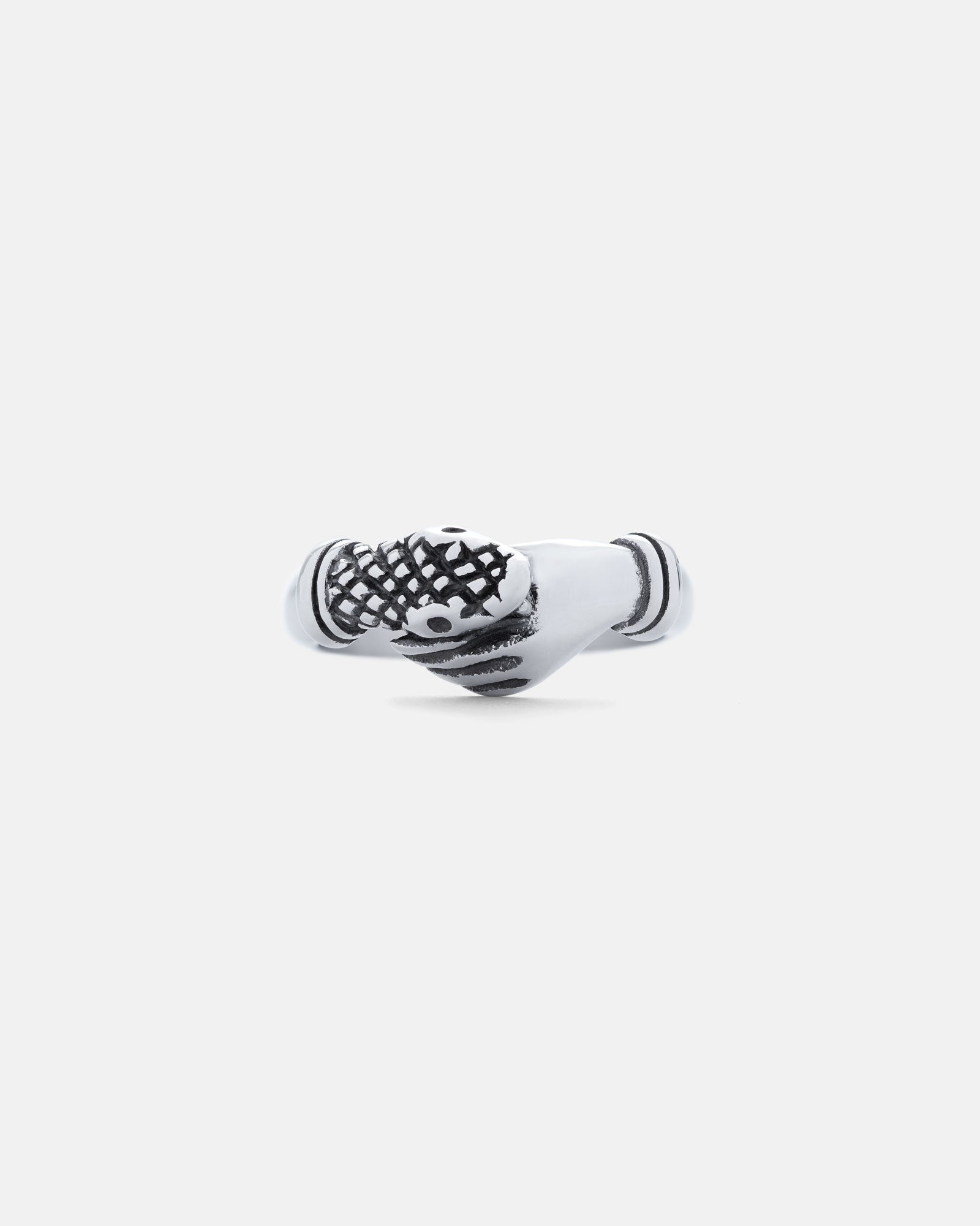 The Hand That Bites" Ring: a silver ring with two clasped hands—one detailed with a crosshatch pattern and black accents—shown on a plain light gray background.