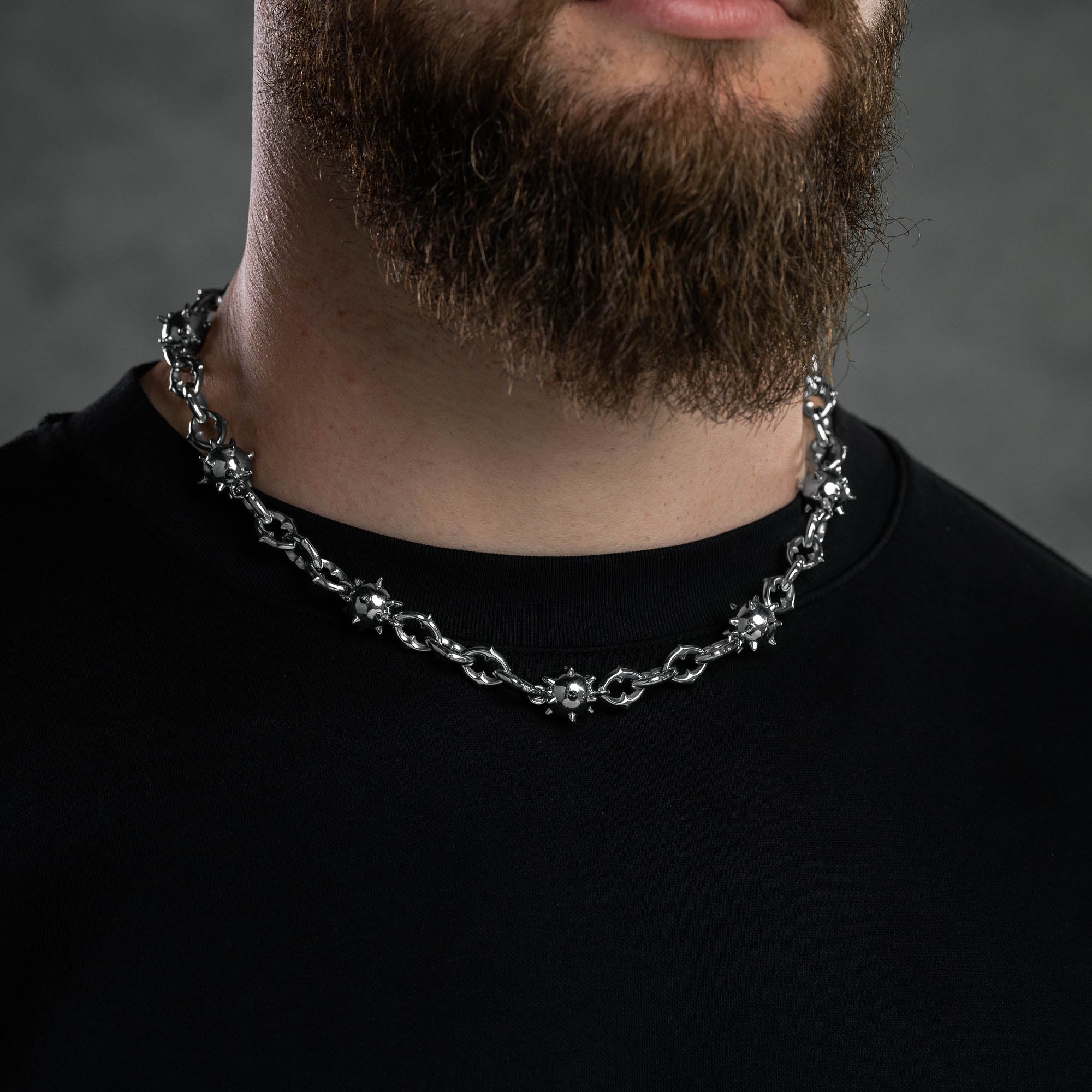 Man with bear wearing silver spiked ball necklace chain against dark background