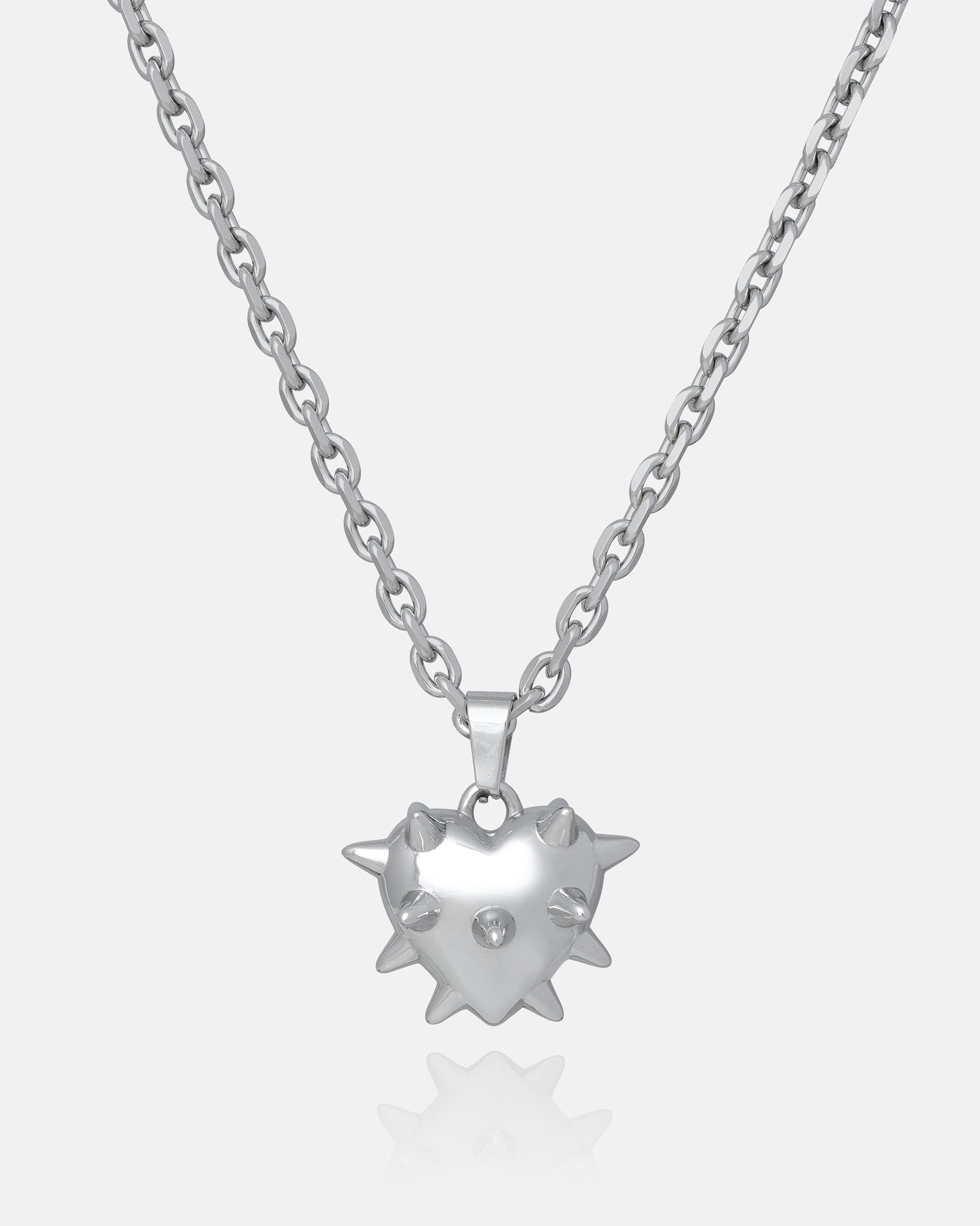 The "Love Hurts" Spiked Heart Pendant is a silver necklace with a shiny heart-shaped pendant, raised spike details, and a central gemstone, shown on a plain white background for an edgy grunge look.