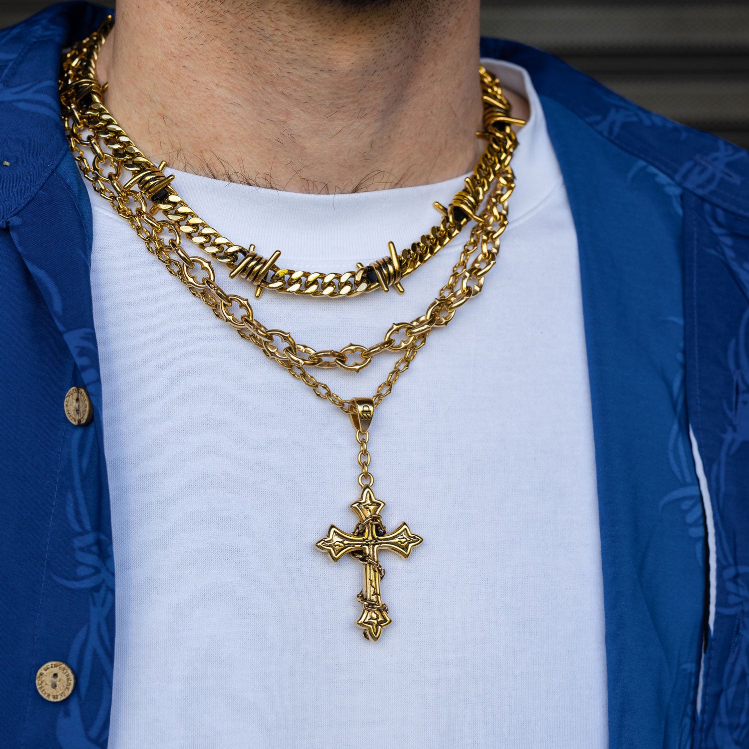 Gold chain set with barbed wire chain and spiked jewelry with cross pendant on mans neck by Statement Collective