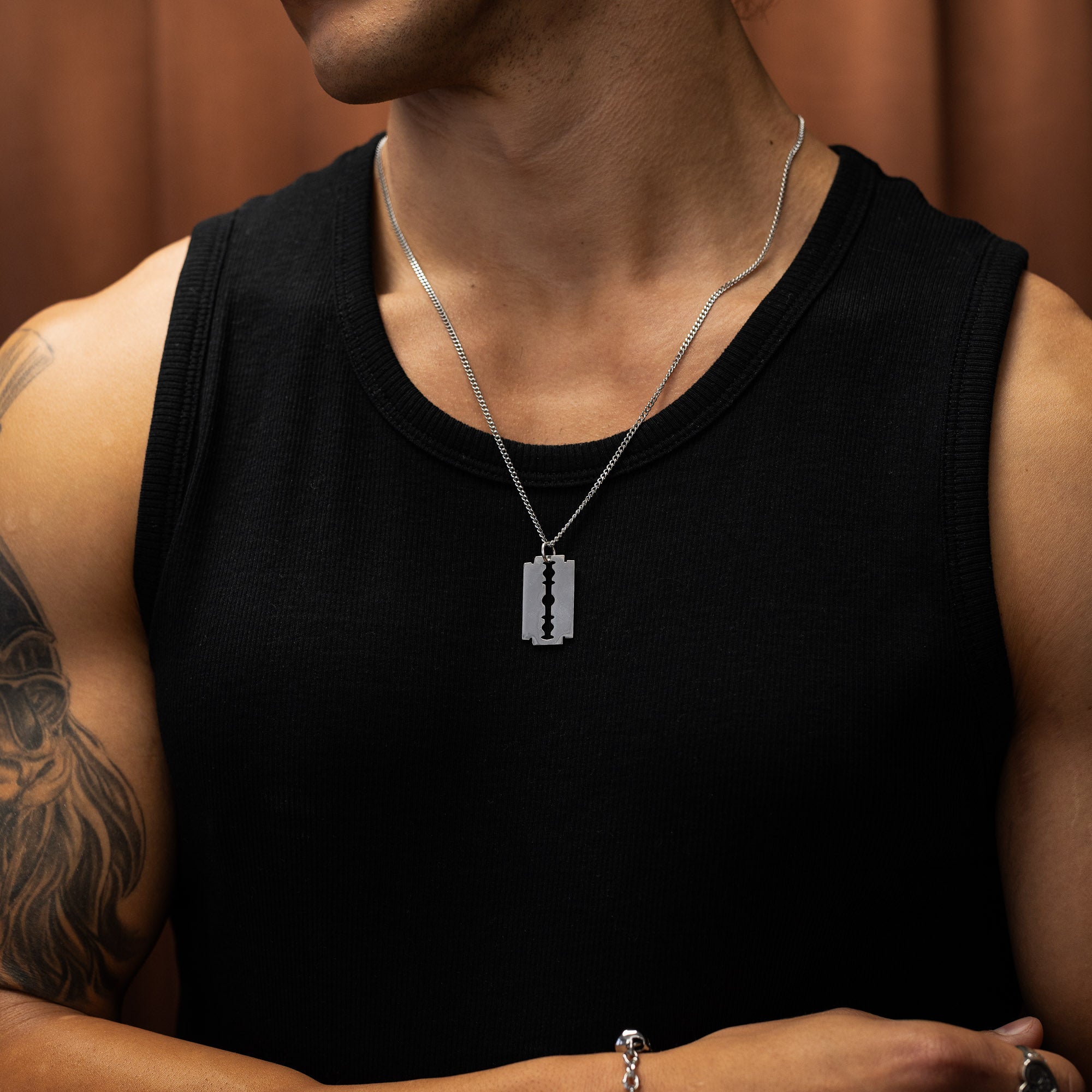 Man wearing a black tank top with a silver necklace featuring a razorblade pendant.