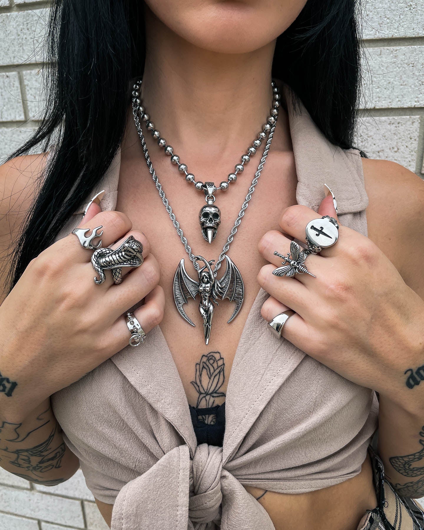 A woman with long dark hair wears "The Enchantress" Pendant, a stainless steel necklace. She also wears several hand carved rings, and tattoos are visible on her chest and hands.