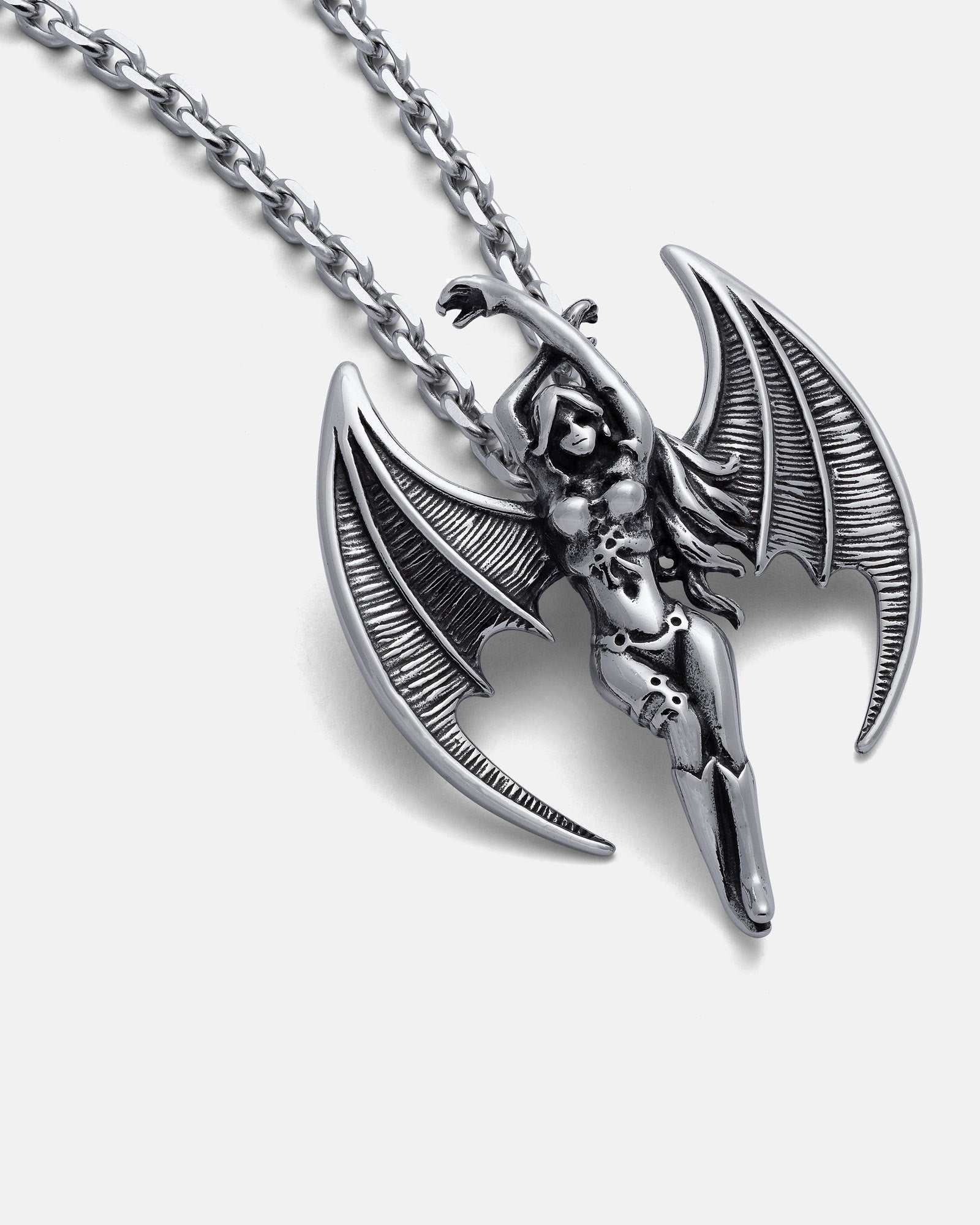 The Enchantress" Pendant is a silver hand-carved necklace with a succubus design, featuring detailed bat-like wings and an intricate body, displayed on a textured chain against a white background.