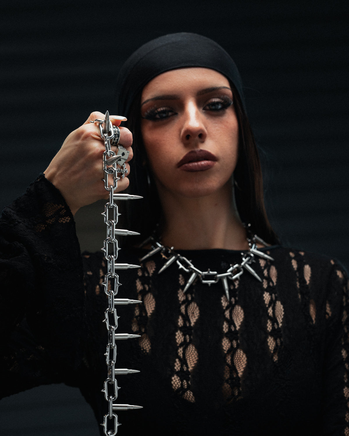 A person wearing a necklace and holding up a matching 15mm Statement Collective Sweating Bullets Necklace Chain made of connected silver bullet-shaped links.