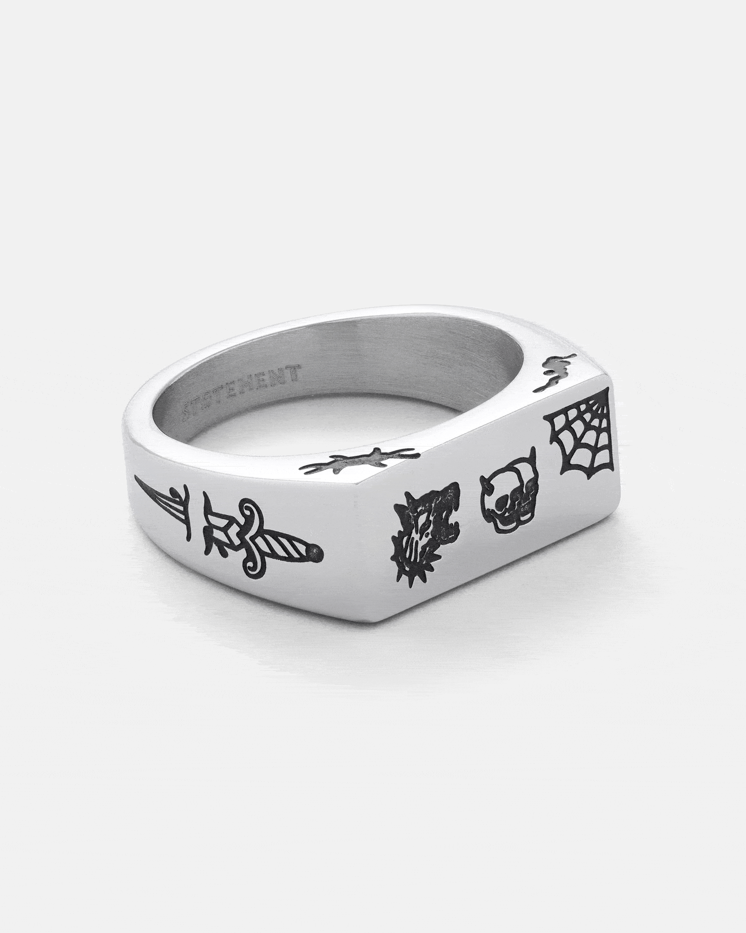 Introducing the Tattoo Signet Ring by STATEMENT—a silver square engraved signet ring featuring striking black engravings of a dagger, burst, skull, and spiderweb on the front and sides. This standout piece embodies the bold, edgy aesthetic of a tattoo signet ring, ideal for those who value unique style and meaningful details.