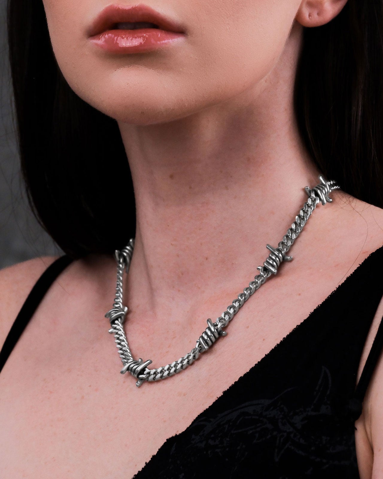 A woman models the 6mm Barbed Wire Cuban Chain necklace with a black top, photographed from the shoulders up against a dark background.