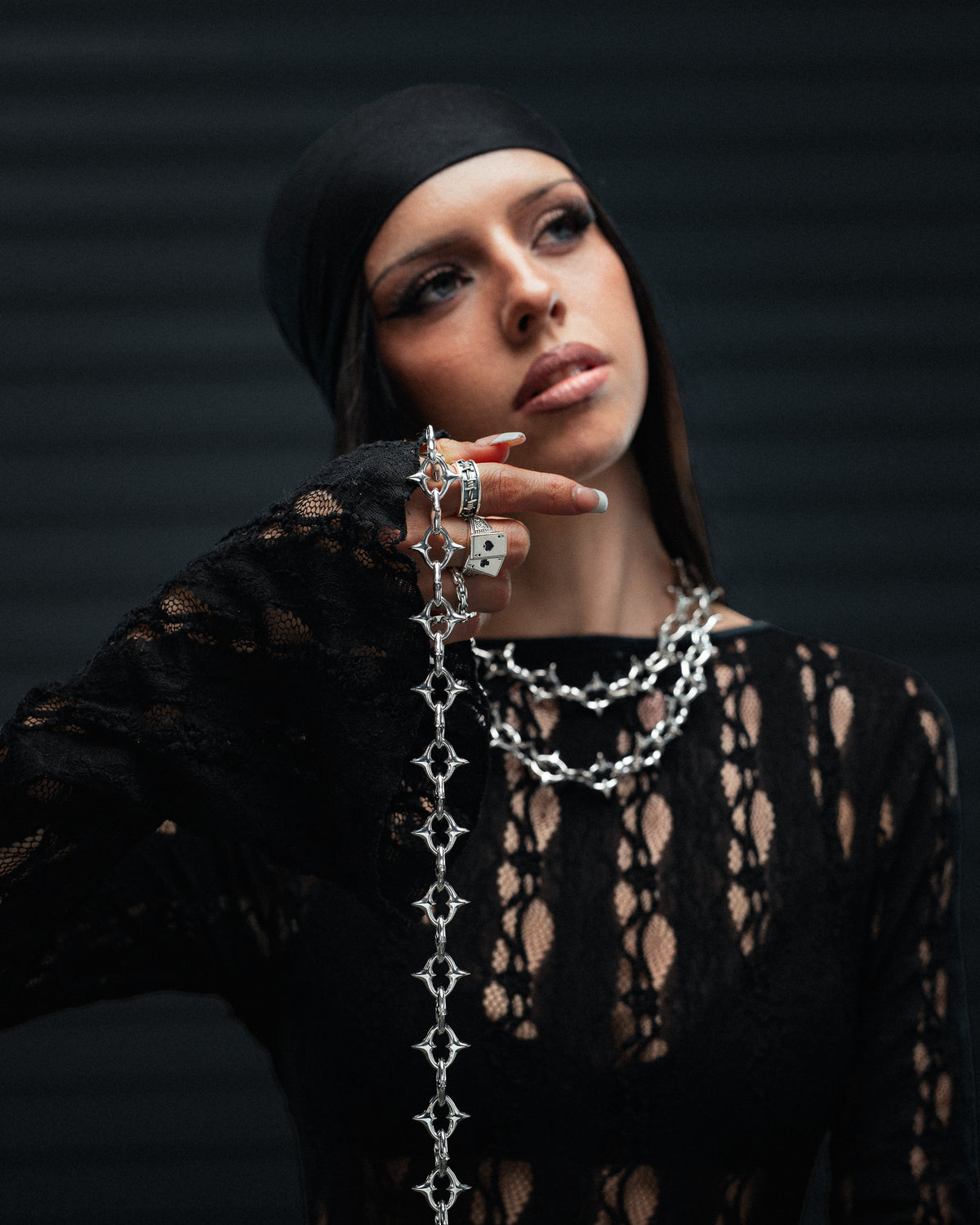 A person wearing an XL The Cathedral 15mm Spiked Chain, a stainless steel gothic necklace with spiked links, draped over one finger.