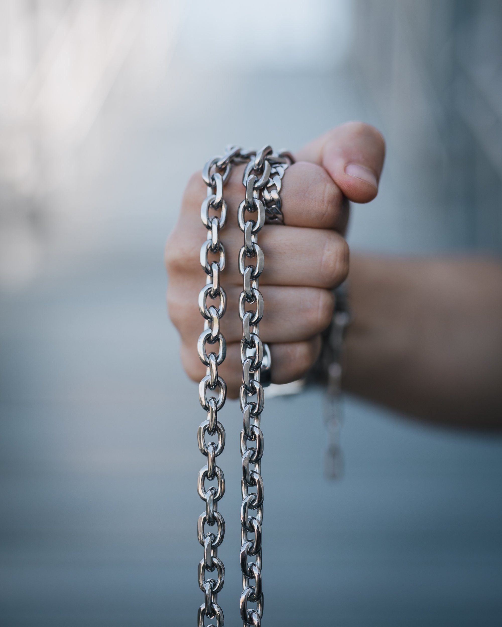 mens hand holding thick cable link necklace with blue background