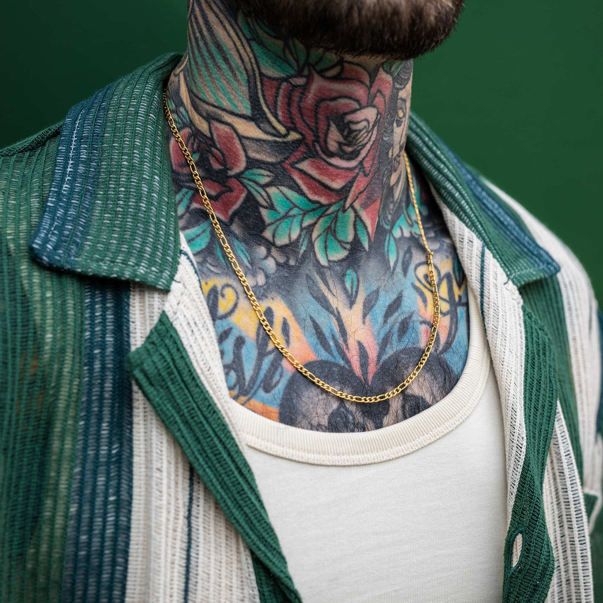 Long gold figaro chain on male model with tattoos